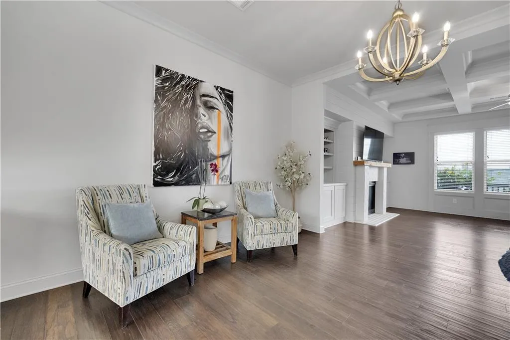 Living area with coffered ceiling, beam ceiling, wood finished floors, ornamental molding, and a fireplace