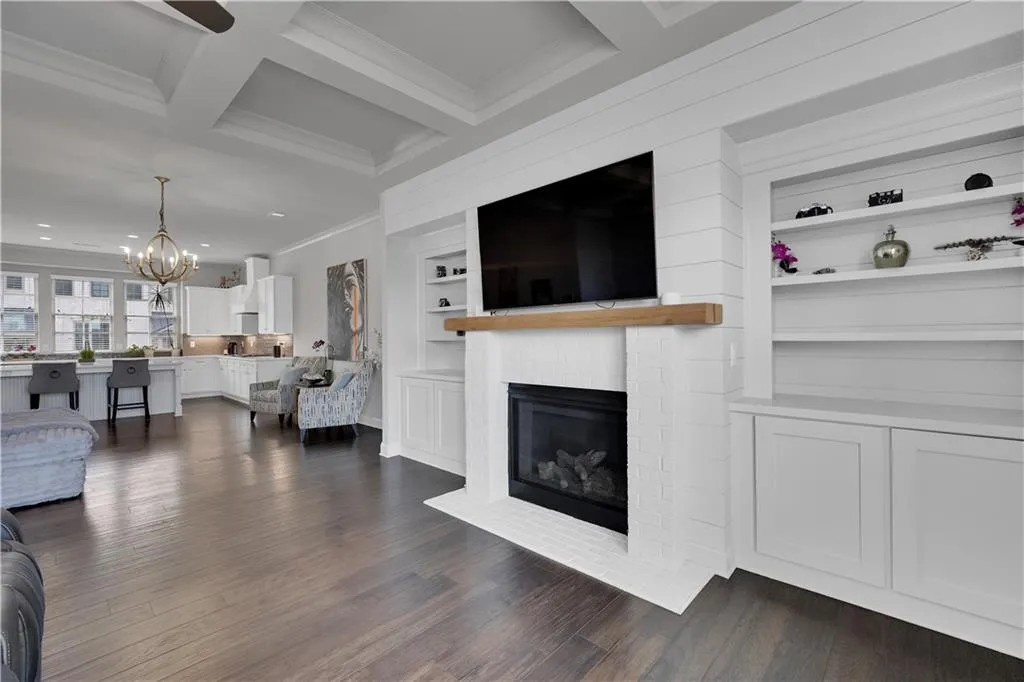 Living room featuring ornamental molding, a brick fireplace, dark wood finished floors, a chandelier, and beamed ceiling