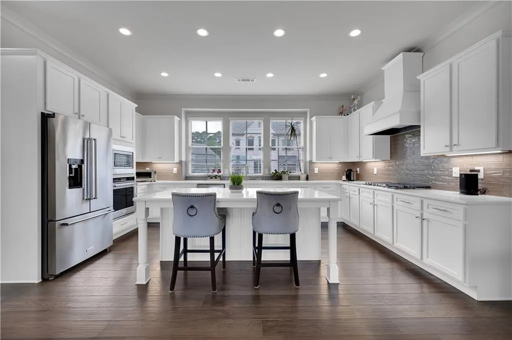 Kitchen with ornamental molding, decorative backsplash, a kitchen bar, appliances with stainless steel finishes, and white cabinets