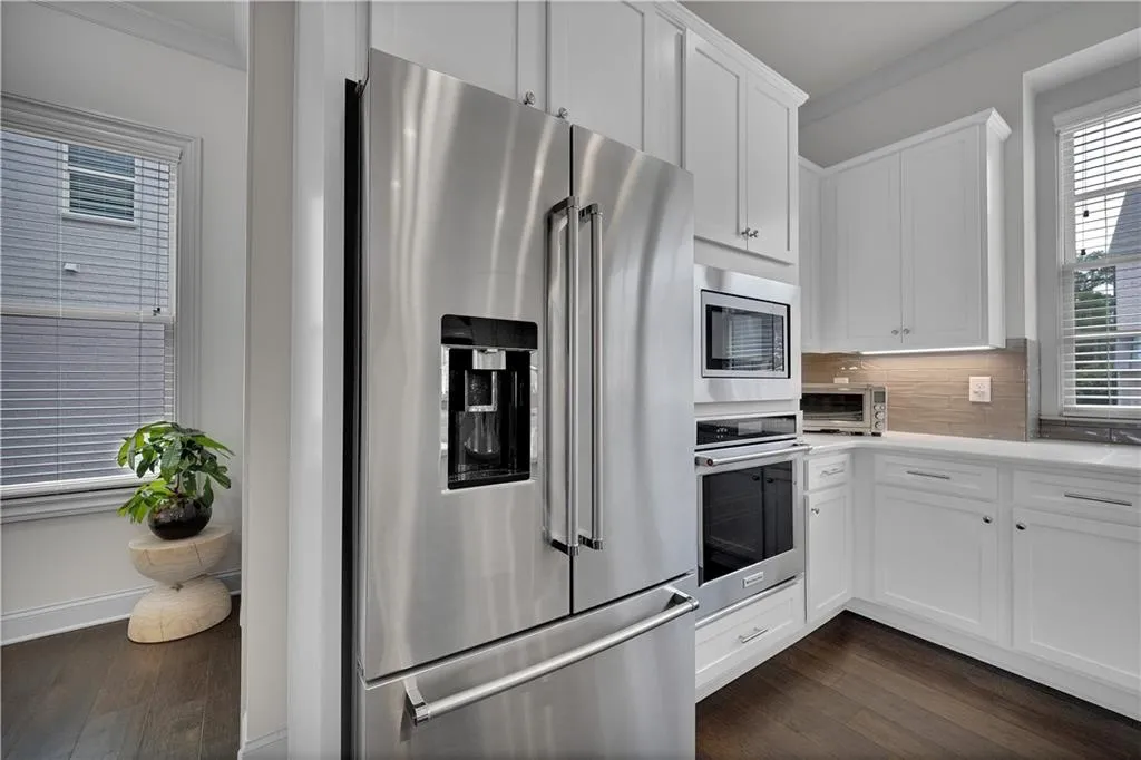 Kitchen featuring stainless steel appliances, white cabinetry, dark wood-style flooring, and crown molding