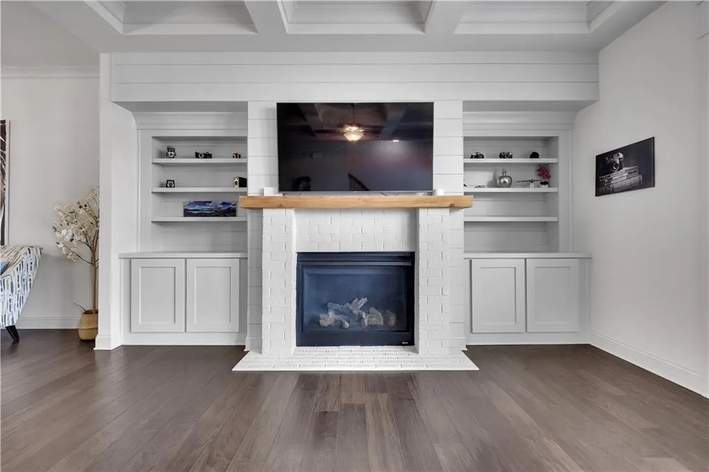 Unfurnished living room featuring dark wood-style floors, built in shelves, a brick fireplace, and beamed ceiling
