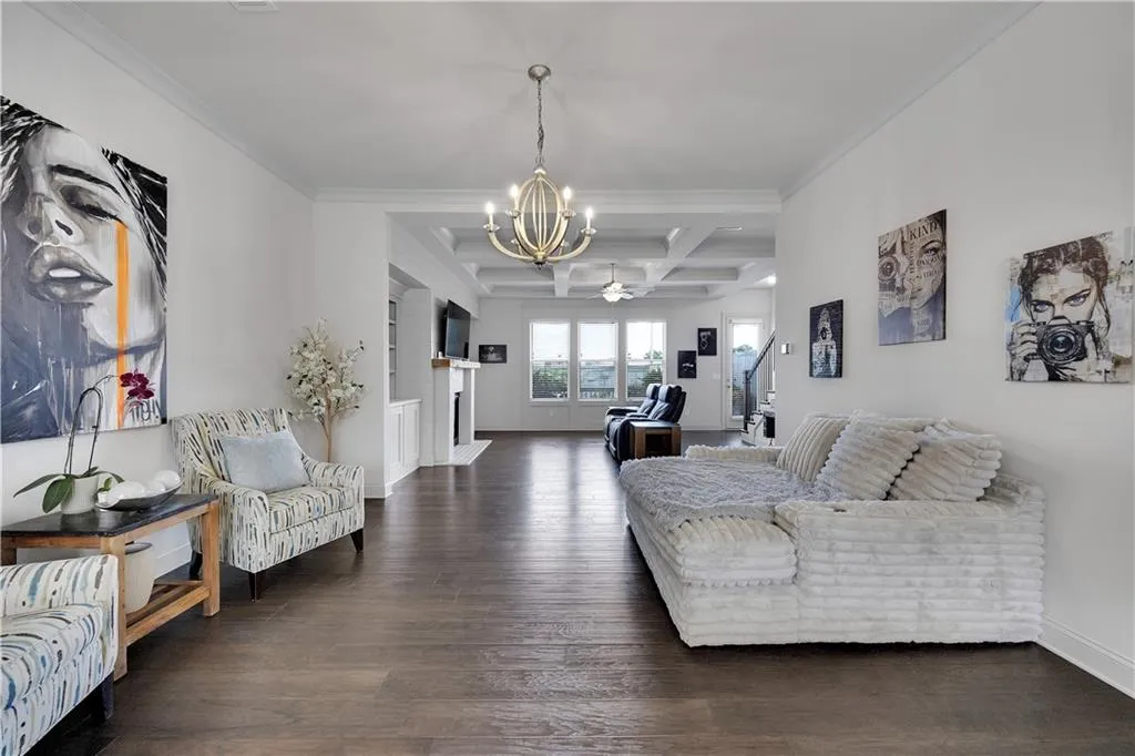 Living room featuring coffered ceiling, beam ceiling, dark wood-style floors, a chandelier, and ornamental molding