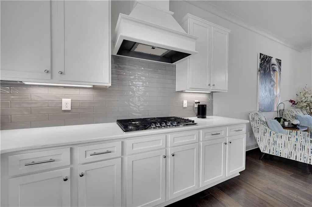Kitchen featuring white cabinetry, premium range hood, tasteful backsplash, ornamental molding, and dark wood-style flooring