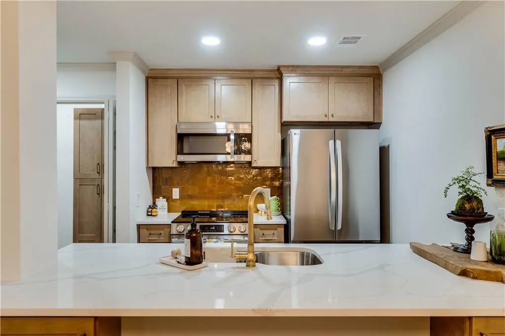 Kitchen with stainless steel appliances, crown molding, and light stone counters