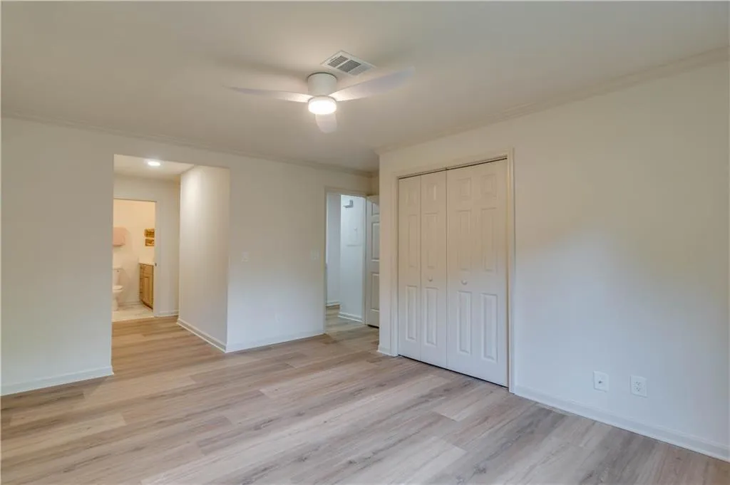Unfurnished bedroom with a closet, ensuite bath, ceiling fan, and light hardwood / wood-style floors