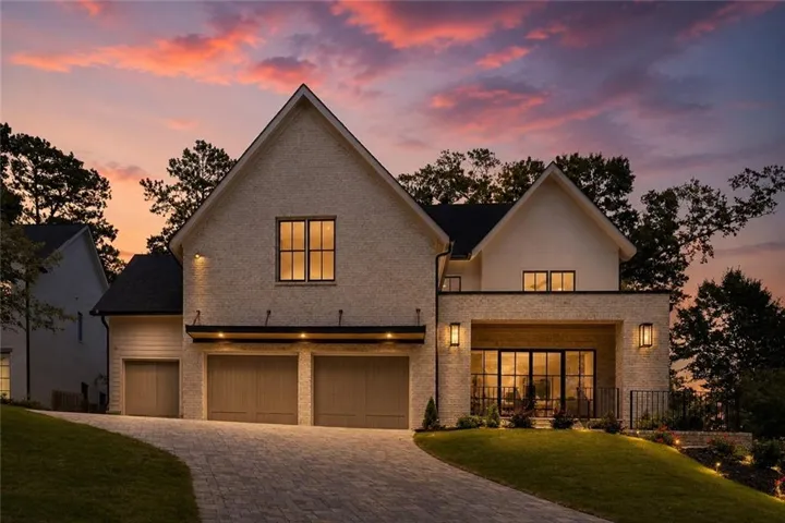 Transitional brick and siding residence featuring a two-car garage, a paver driveway, and an upper-level balcony