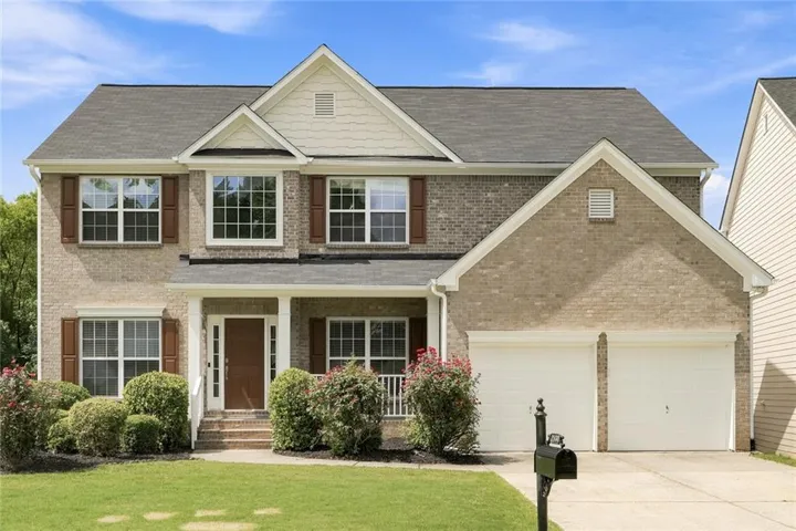 Brick-front residence featuring a covered front porch, white columns, and a dark wood front door