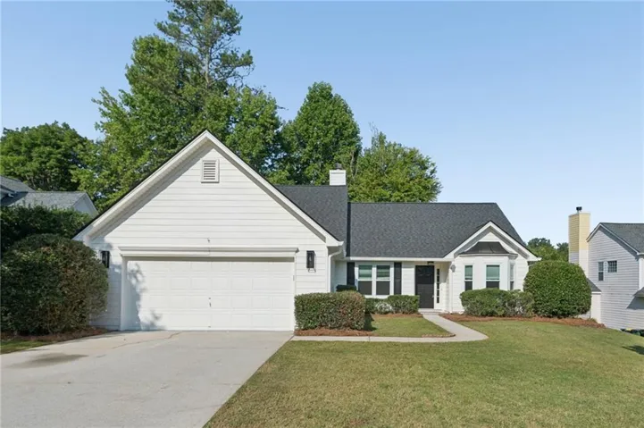 White siding exterior with a dark shingle roof, attached garage, paved driveway, and mature landscaping