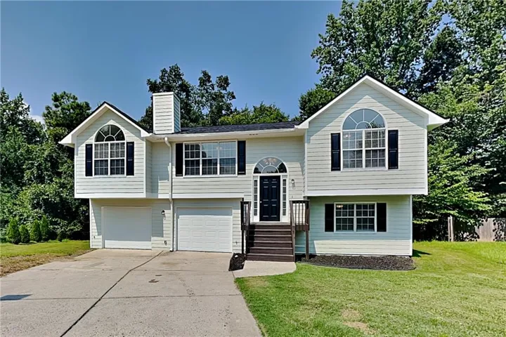 Split-level residence featuring light-colored siding, dark shutters, and a prominent front entry staircase