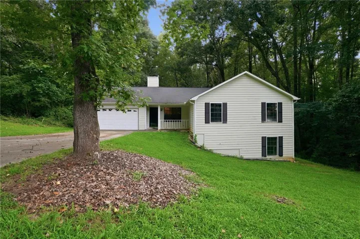 White siding exterior with black shutters, attached garage, covered porch, and mature trees