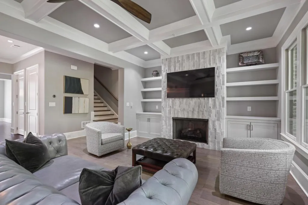 Living room featuring wood finished floors, a premium fireplace, coffered ceiling, built in shelves, and recessed lighting