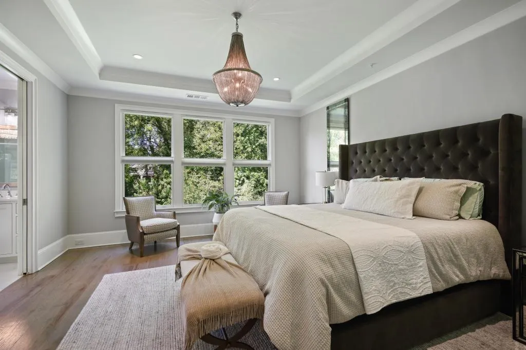 Bedroom with light wood-style floors, ensuite bathroom, ornamental molding, a chandelier, and a tray ceiling
