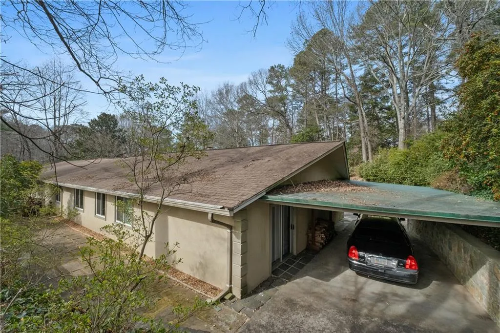 View of side of property featuring stucco siding, an attached carport, a shingled roof, and driveway