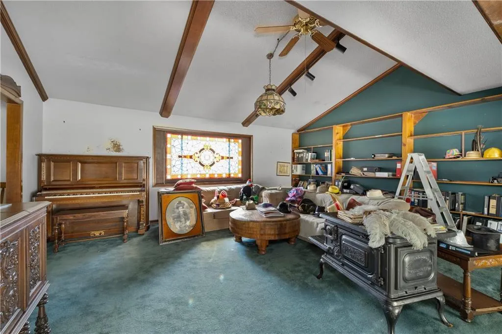 Living area with dark colored carpet, beamed ceiling, ceiling fan, and high vaulted ceiling
