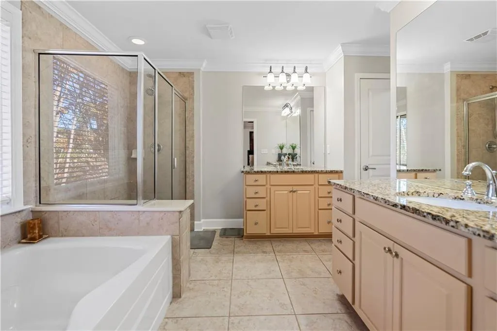 Full bath featuring a garden tub, ornamental molding, a stall shower, two vanities, and light tile patterned floors