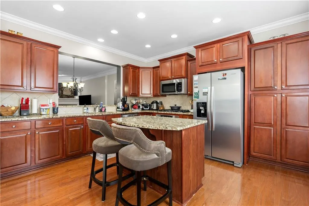 Kitchen featuring ornamental molding, appliances with stainless steel finishes, light stone counters, a kitchen bar, and light wood-style flooring