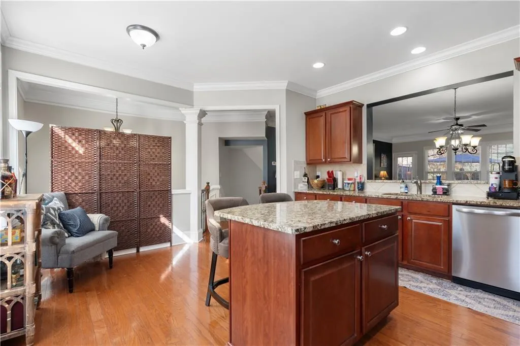 Kitchen with a breakfast bar area, ornamental molding, light stone countertops, stainless steel dishwasher, and pendant lighting