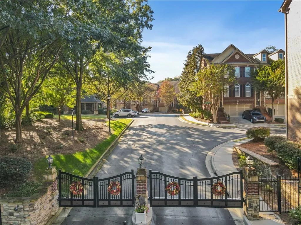 View of asphalt street featuring street lighting, curbs, and a gated entry