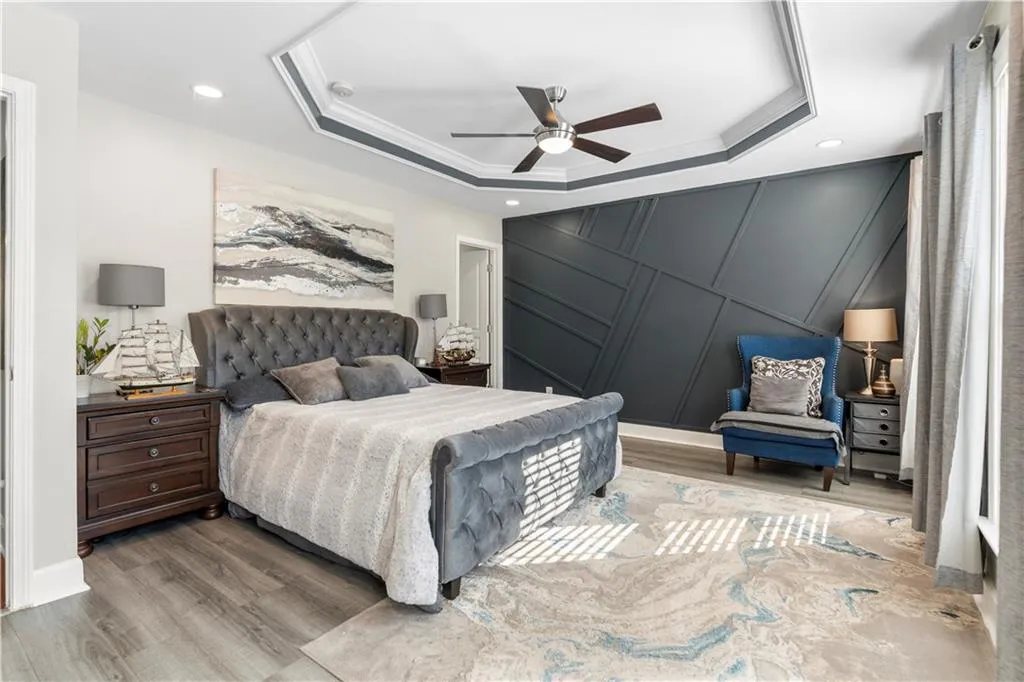Bedroom with wood finished floors, ceiling fan, a tray ceiling, recessed lighting, and crown molding