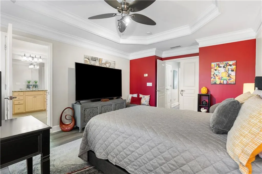 Bedroom featuring ensuite bathroom, a tray ceiling, crown molding, a ceiling fan, and wood finished floors