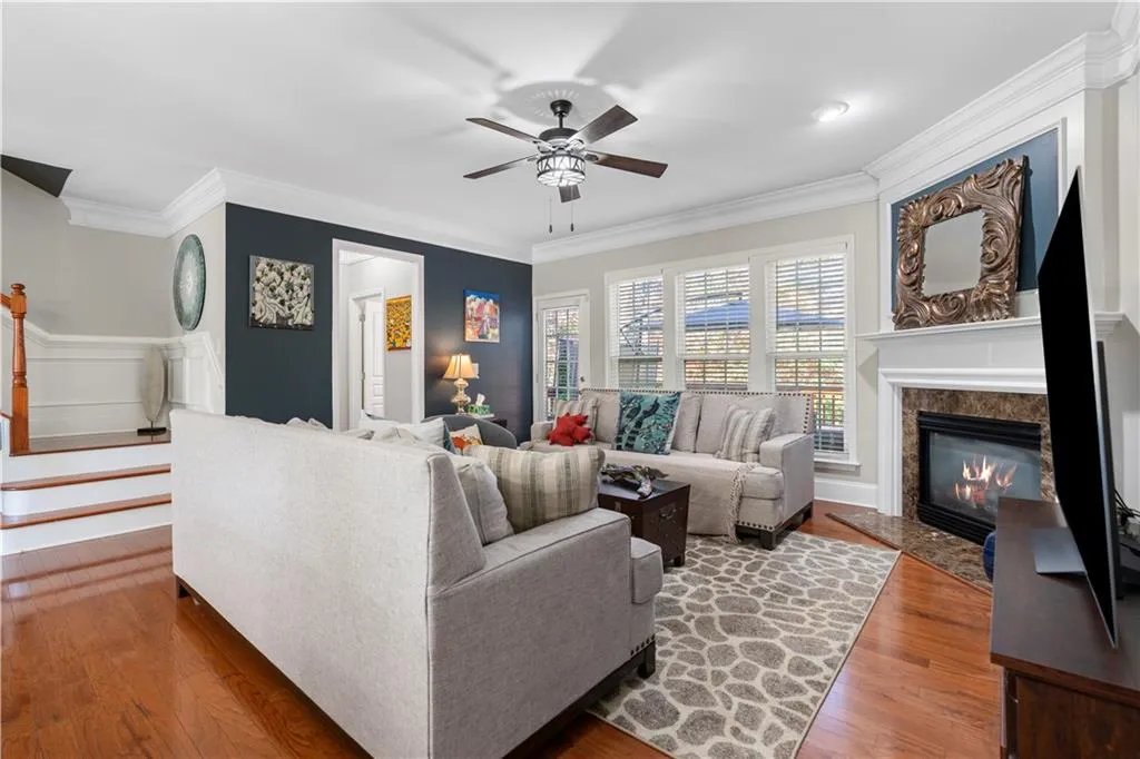 Living room with ornamental molding, a high end fireplace, wood finished floors, a ceiling fan, and stairway