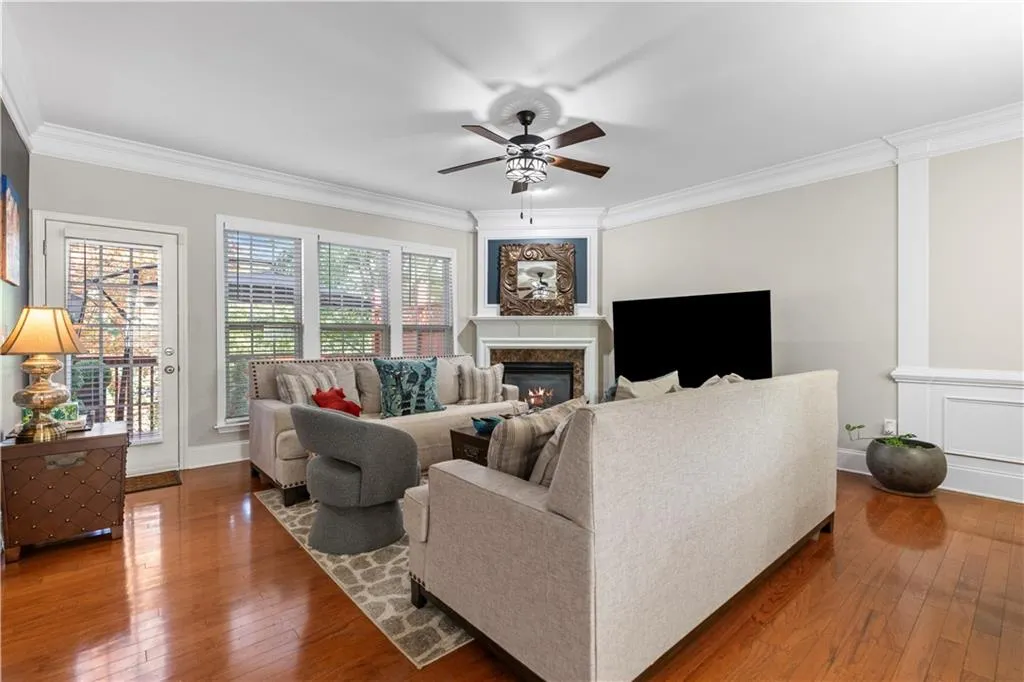 Living area featuring wood-style flooring, a covered fireplace, ornamental molding, and a ceiling fan