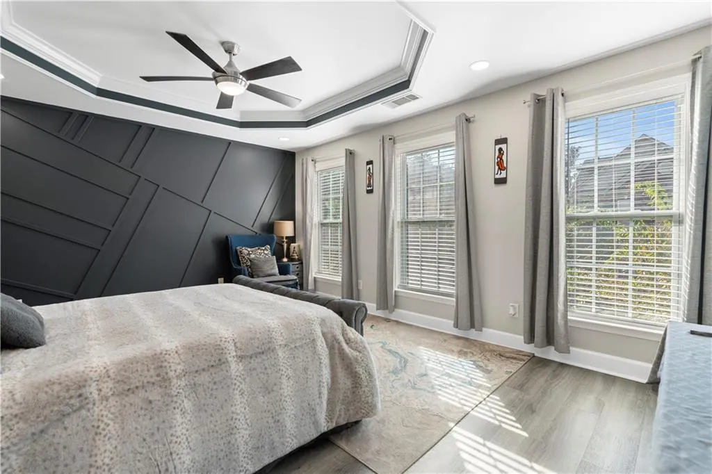 Bedroom with a ceiling fan, a tray ceiling, light wood-style floors, ornamental molding, and recessed lighting