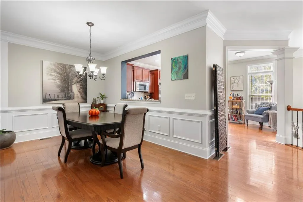 Dining area featuring ornamental molding, light wood-style flooring, a decorative wall, wainscoting, and a chandelier