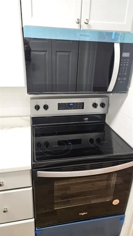 Kitchen view of appliances with stainless steel finishes, white cabinets, decorative backsplash, and a warming drawer