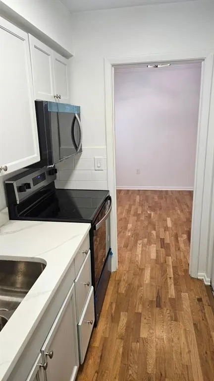 Kitchen featuring stainless steel range with electric stovetop, white cabinetry, light wood finished floors, black microwave, and light stone counters