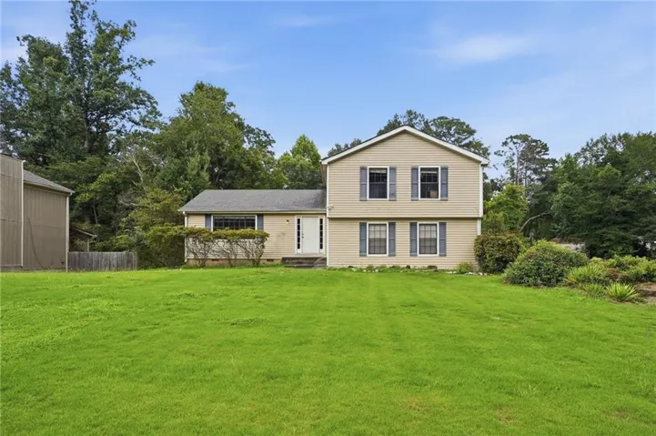 Two-story split-level home with beige siding, dark shutters, and a front entry with white steps