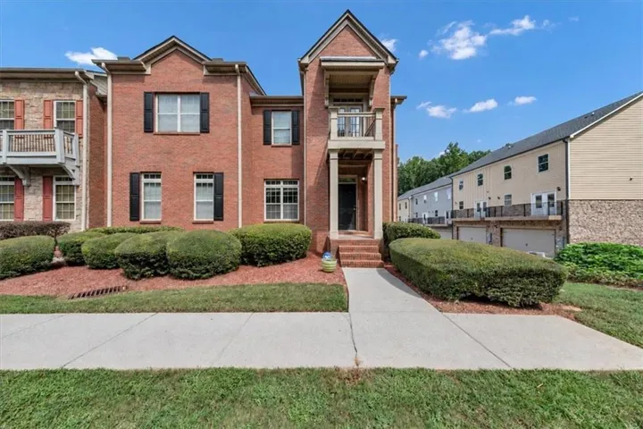 Brick exterior with a covered entryway, upper-level balcony, and mature landscaping
