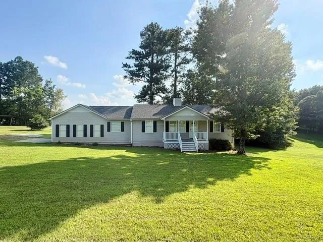 Expansive front lawn with mature trees, a covered front porch, and a gray siding exterior with dark shutters