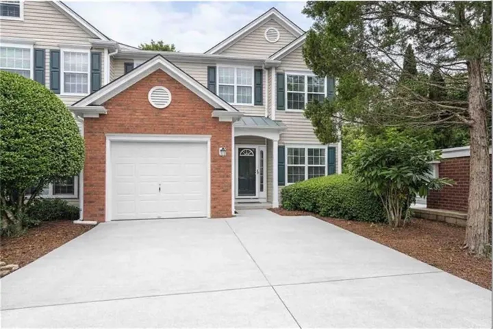 Brick and siding exterior with a pitched roofline, attached garage, concrete driveway, and mature landscaping