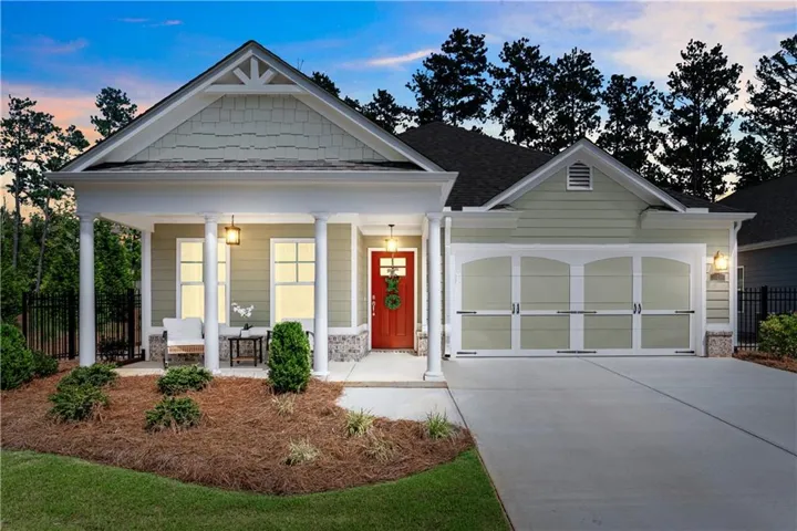 Inviting covered front porch with white columns, red entry door, decorative garage door, stone accent details, and a concrete driveway