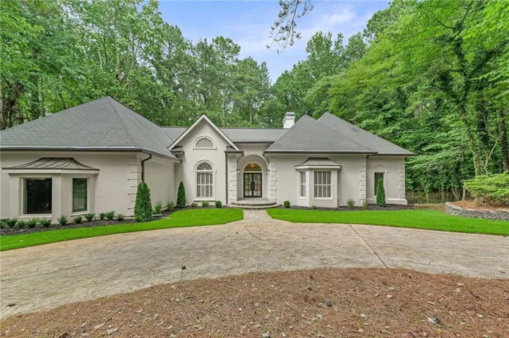 Stucco exterior featuring a prominent arched entry with double doors, symmetrical bay windows, and a multi-gabled roofline