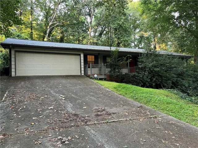 Exterior featuring an attached garage, covered front porch, and mature landscaping
