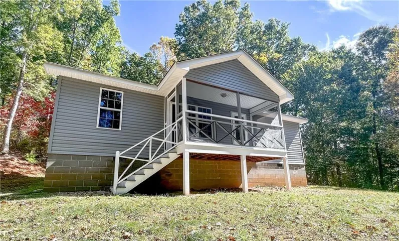 Single-story residence featuring gray siding, a screened porch with white railings, and a concrete block foundation