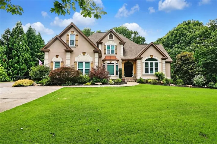 Stucco exterior with stone accents, multiple gables, arched entry, bay window, and manicured landscaping
