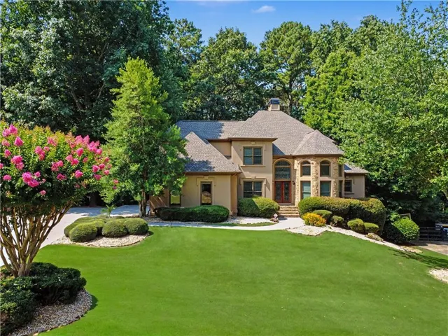 Stately stucco and stone exterior featuring a prominent two-story arched entry with double doors, symmetrical windows, a hip roofline, and established landscaping with mature trees