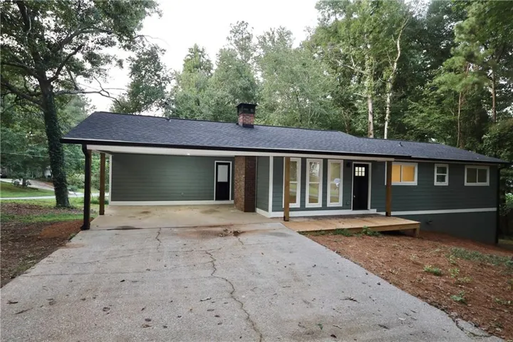Ranch-style exterior with dark green siding, a black shingle roof, and a red brick chimney