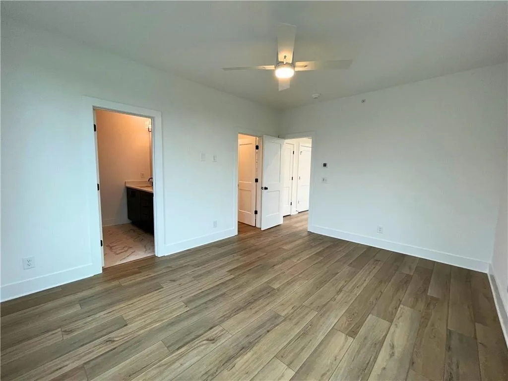 Unfurnished bedroom with dark wood-style floors, a ceiling fan, and ensuite bath
