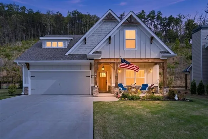 Craftsman-style home featuring a covered front porch with stone-clad columns and exposed timber beams, a two-car garage with an overhead dormer, and a board and batten facade with shingle accents
