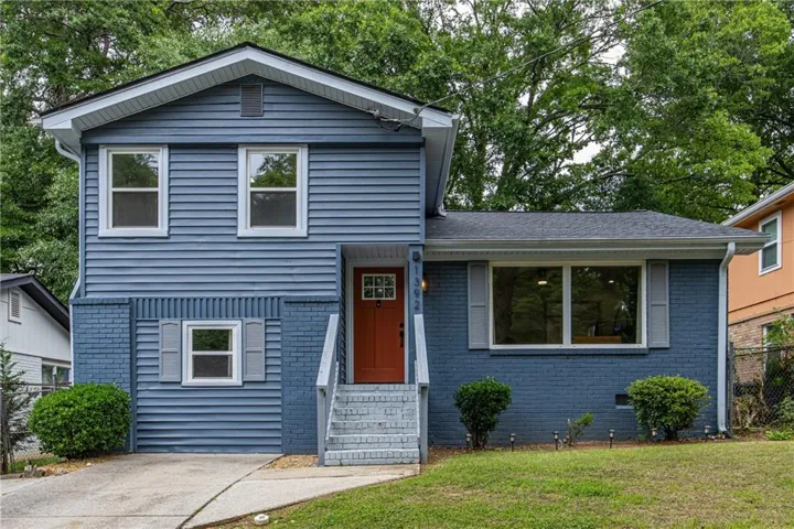 Split-level exterior featuring blue siding and brick, a vibrant orange front door, white window frames, and a gray shingle roof