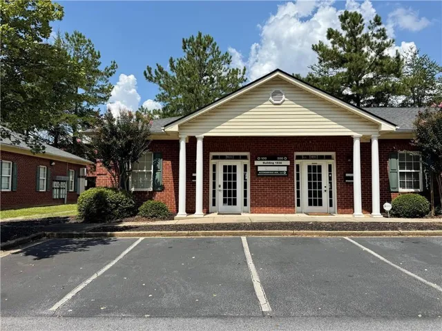 Brick facade with white double entry doors, columned portico, gable roof, and asphalt parking