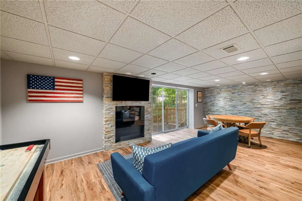 Living area with a drop ceiling, a stone fireplace, and wood finished floors