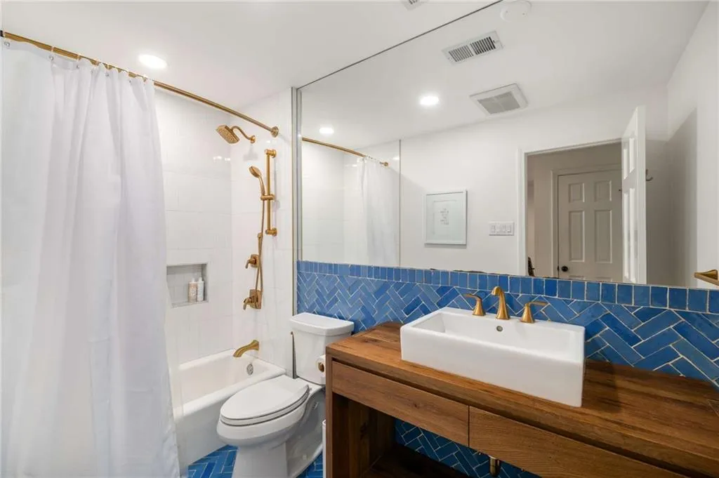 Bathroom featuring tile walls, vanity, shower / bath combo, recessed lighting, and wainscoting