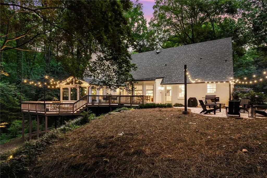 Back of property at dusk with a wooden deck, roof with shingles, and a patio