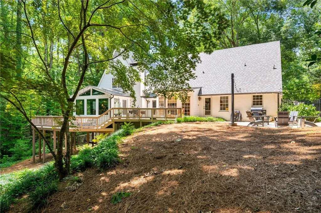 Back of house featuring a deck, roof with shingles, a patio area, and brick siding