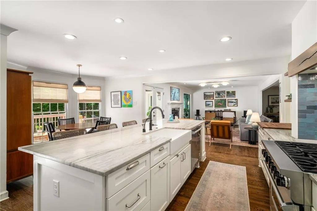 Kitchen with appliances with stainless steel finishes, a fireplace, light stone counters, white cabinets, and a kitchen island with sink